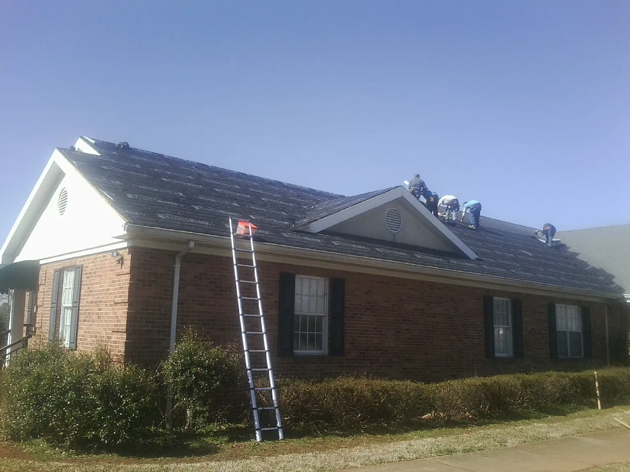 Crew tearing shingles off a brick ranch roof with a ladder set — Metal Roof Repair work by our crew in King Of Prussia