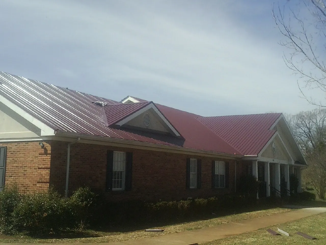 Red metal roof with gabled entries on a long brick building, from a Hail Damage Roof Repair job in King Of Prussia