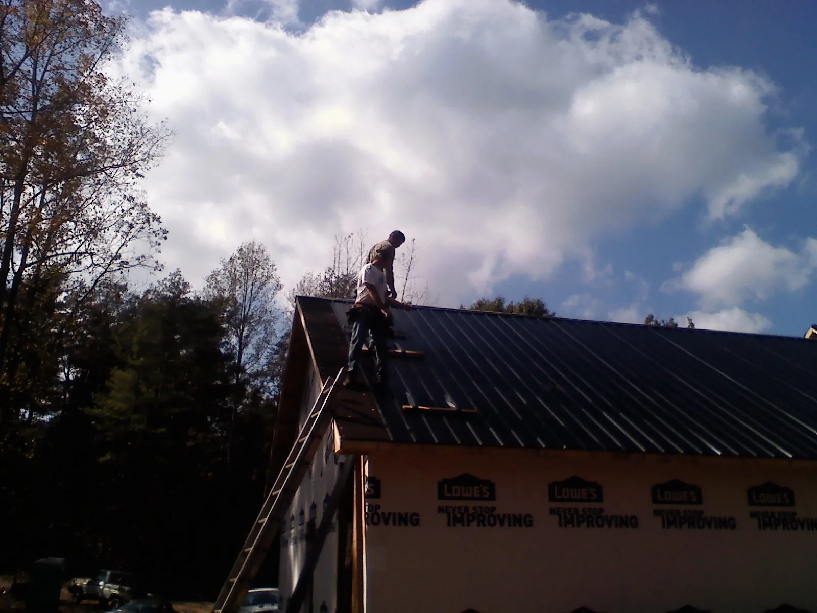 Roofer fastening dark metal panels high against a cloudy sky, from a Roof Inspection job in King Of Prussia