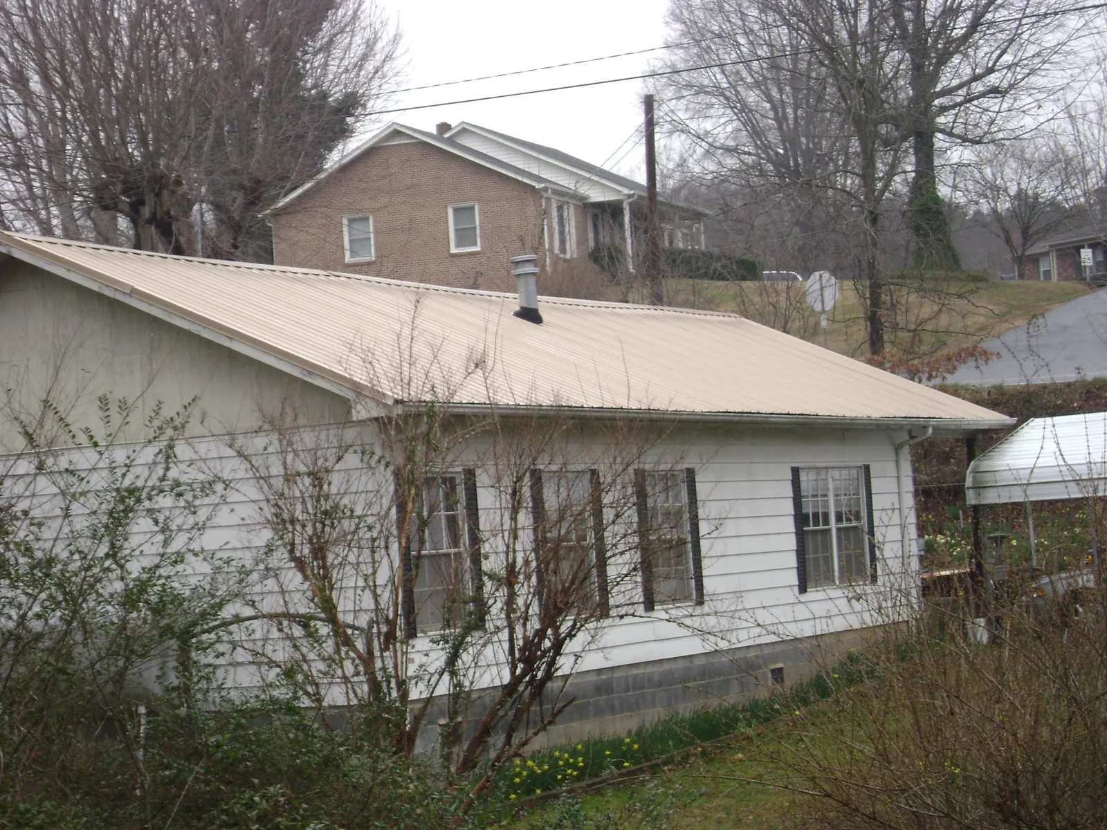 Tan metal roof on a white sided house set into a hillside — Commercial Roofing by Roofing Brothers in King Of Prussia
